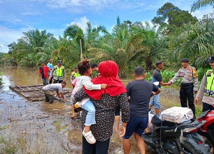 Satsamapta Polres Aceh Jaya Terjun Langsung Membantu Masyarakat Menyeberangkan Jalan Akibat Tergenang Air Hujan